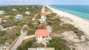 A coastal property with a long stretch of beach, a road leading to the beach, and a series of buildings with red roofs.