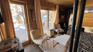 A cozy cabin interior with a white armchair, a small table, and a zebra-patterned bed.