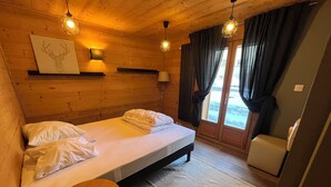 A cozy wooden room with a bed, a small round table, and a window with curtains.