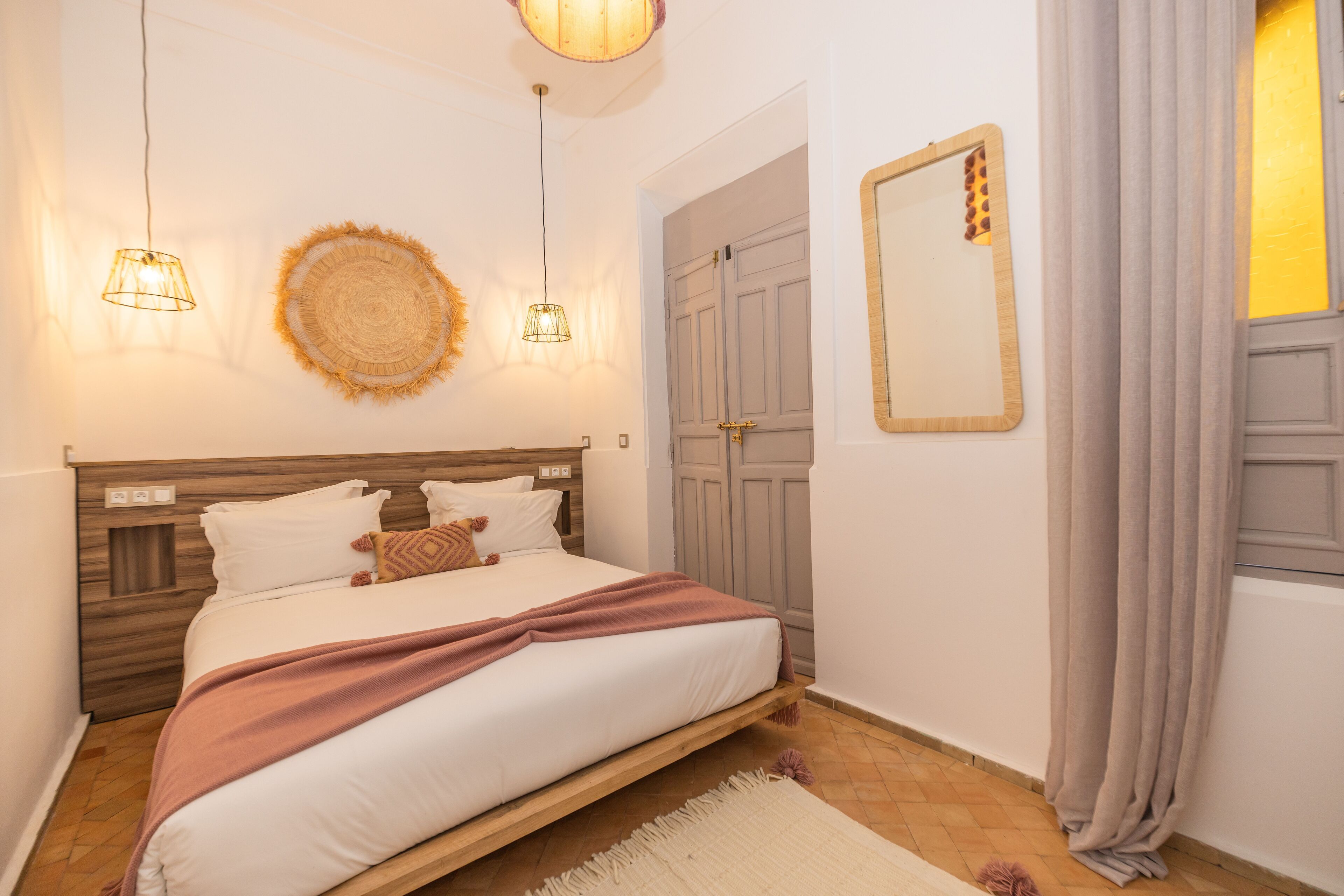 A bedroom with a bed, bedside lamps, a mirror, and a door.