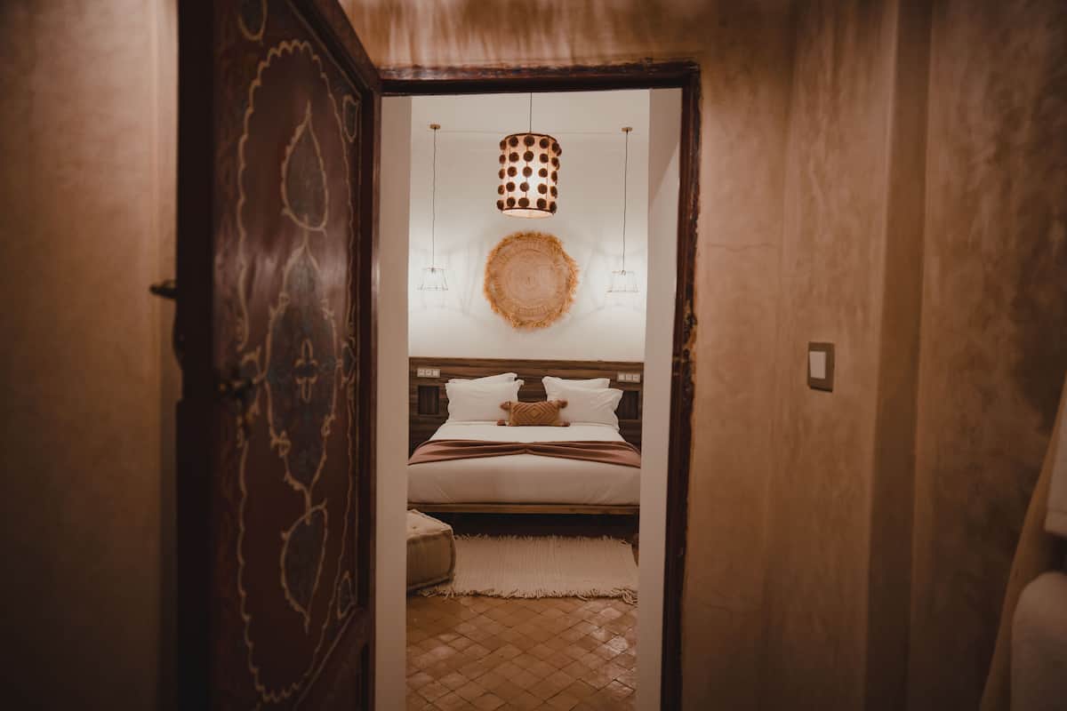 A bedroom with a wooden headboard, a round woven rug, and a bed with white bedding.