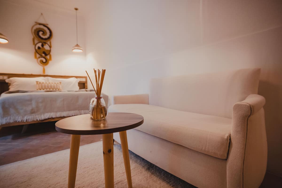 A modern hotel room with a bed, a sofa, a small round table, and a decorative wall piece.