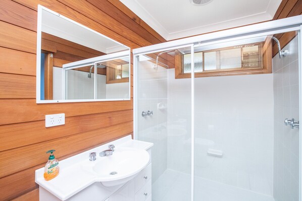 A modern bathroom with wooden paneling, a white sink, and a glass-enclosed shower. - Ironbark - Glorious waterfront (Forster)