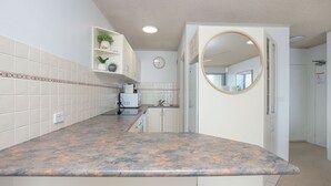 A kitchen with white cabinets, a granite countertop, and a microwave. There is a clock on the wall and a mirror above the sink. - Oceanic 7 - Opposite from main beach (Forster)
