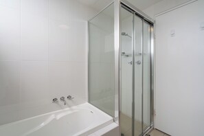 Une salle de bain avec une douche à parois de verre, une baignoire blanche et des murs recouverts de carreaux blancs.