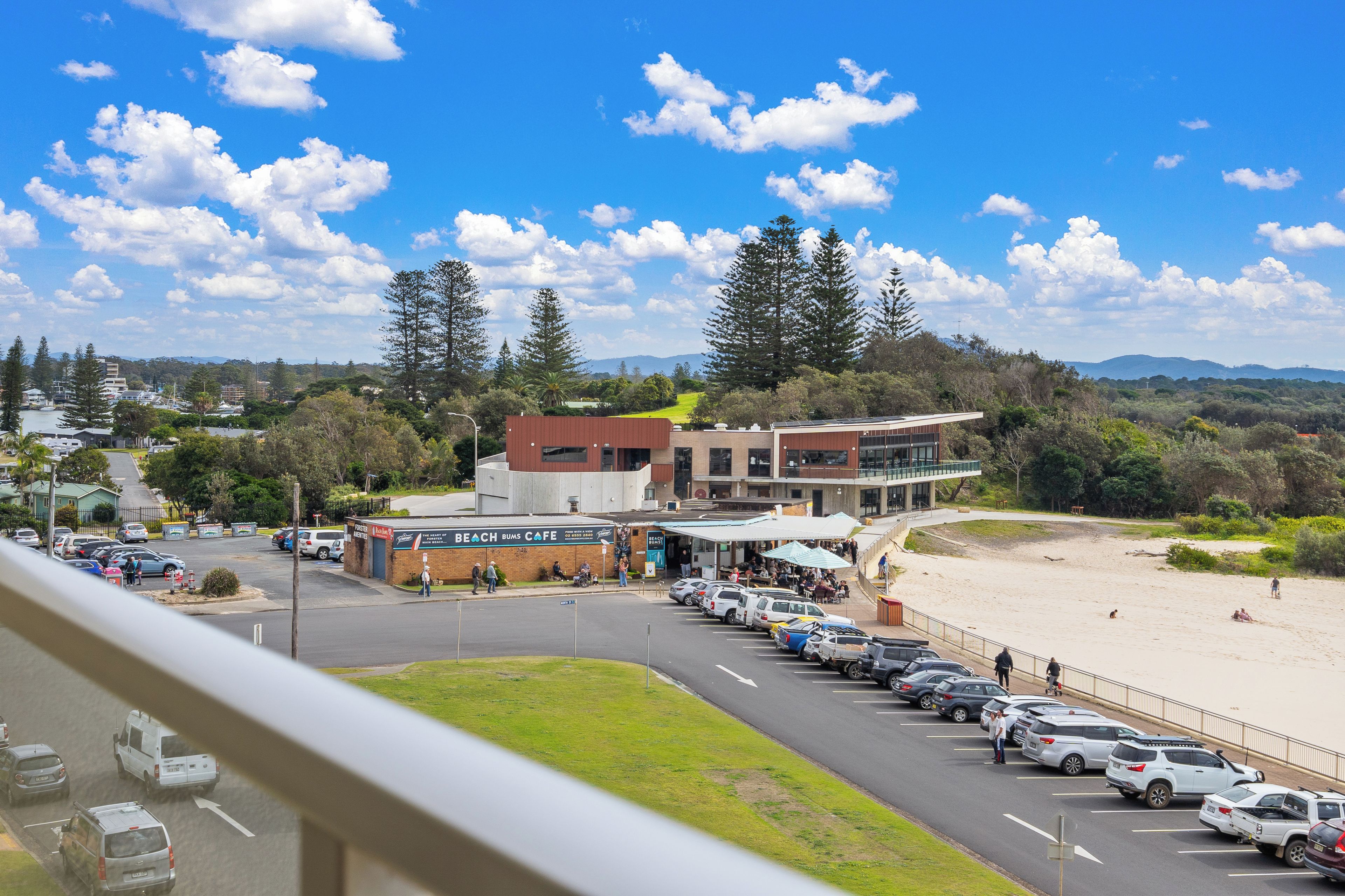 A coastal view with a beach, parked cars, and a building with a sign for a cafe.