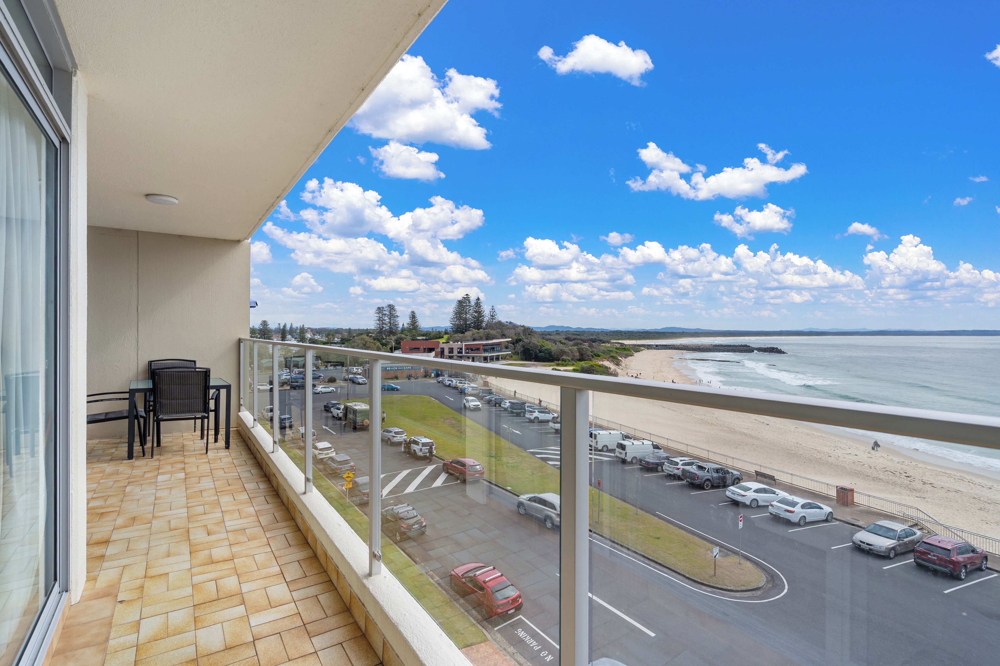 Een balkon met uitzicht op een strand en parkeerplaats.