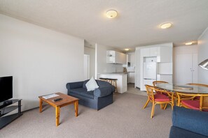 Un espace de vie compact comprenant un canapé, une table basse, un téléviseur, un coin cuisine et un espace repas.
