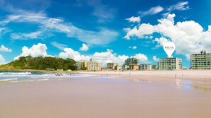A beach with a hotel named "RELAY." There are buildings along the shore and a forested hill in the background.