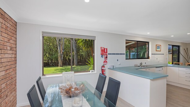 A modern kitchen with a glass dining table, black chairs, and a view of the outdoors. - Spacious. Tropical. Waterfront. (Tuncurry)