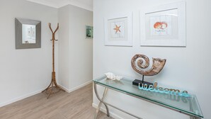 A reception area with a glass console table displaying a 'welcome' sign, framed artwork, and a wooden coat stand. - Spacious. Tropical. Waterfront. (Tuncurry)