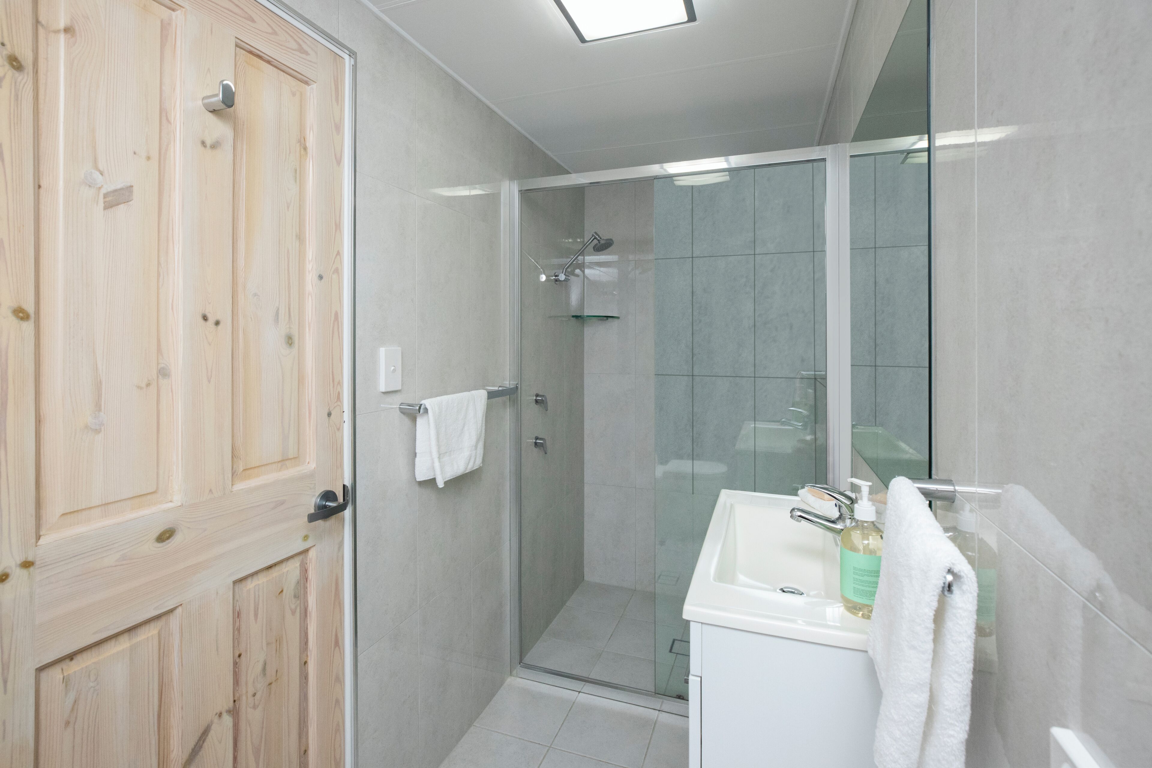 Een moderne badkamer met een douchecabine van glas, een wit wastafelmeubel en een houten deur.