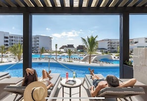 A poolside area with lounge chairs and a view of a resort pool and buildings. - *THIS XMAS!* Amazing 3 BR resort vacation in Mexico (Puerto Morelos)