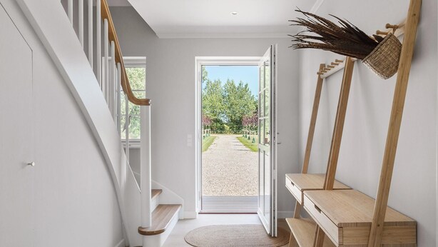 Un couloir avec un escalier en bois, un banc et une porte donnant sur un espace extérieur.