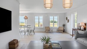 Un vaste salon doté d’un grand téléviseur à écran plat, de deux lampes suspendues en osier, d’un canapé, d’une table basse agrémentée d’une plante et d’un livre, ainsi que d’un coin repas avec une table et des chaises.