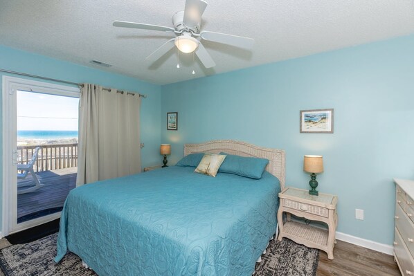 A bedroom with a bed, a ceiling fan, a nightstand, a dresser, and a view of the ocean through a door. - Followin The Son - Amazing 4 BR Oceanfront Duplex; Great Views! (North Topsail Beach)