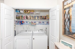 A laundry room with two Whirlpool washers, a shelf with books and board games, and a framed picture on the wall. - Followin The Son - Amazing 4 BR Oceanfront Duplex; Great Views! (North Topsail Beach)