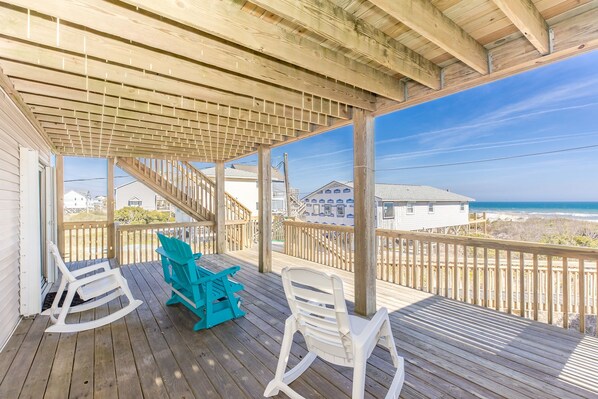 A wooden deck with a covered area, two rocking chairs, and a view of the ocean.