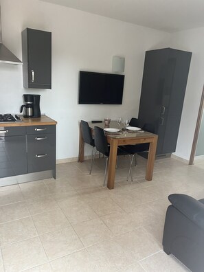 A compact kitchen with a gas stove, a coffee maker, and a TV mounted above a dining table with chairs.