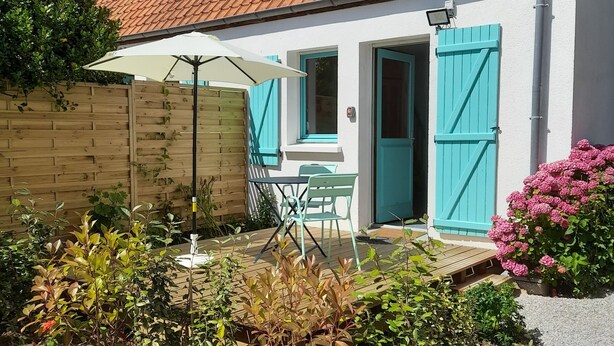 A house with a tiled roof, a wooden fence, and a garden with various plants and flowers.