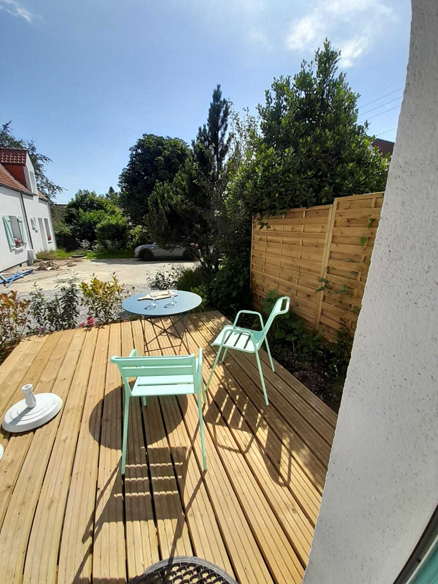 A wooden deck with a round table and two chairs, surrounded by a wooden fence and greenery.