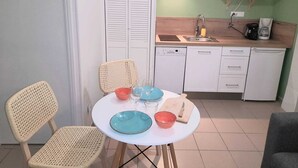 A compact kitchen with a white dishwasher, a microwave, and a coffee maker on the counter. There is a dining table with two chairs and a small cutting board.