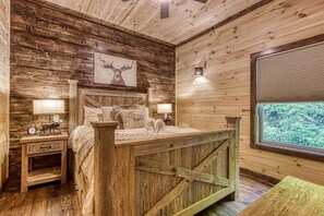 Une chambre à coucher rustique en bois, dotée d’un lit à baldaquin, de lampes de chevet, d’une table de chevet et d’une fenêtre donnant sur un paysage verdoyant.