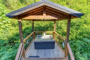 Une structure en bois abritant un bain à remous, dotée d’un toit et entourée d’une végétation luxuriante.