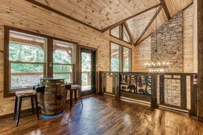 A wooden interior with large windows, a stone wall, and a bar area. - Wiley Bear • Private Bunks + Hot Tub + Game Rm - Chalet Village Gatlinburg (Gatlinburg)