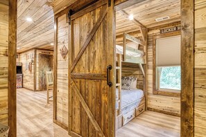 A wooden cabin interior with a bunk bed, a door with a crossbeam design, and a sign reading 'LOCKER ROOM'. - Wiley Bear • Private Bunks + Hot Tub + Game Rm - Chalet Village Gatlinburg (Gatlinburg)