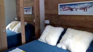 A bedroom with a wooden wall, a bed with blue and white bedding, a mirror, and a painting of a snowy landscape.