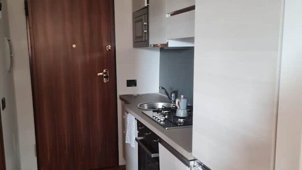 Een kleine keuken met een houten deur, witte kastjes, een ingebouwde oven en een vloerkleed met dessin.