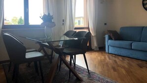 Un salon avec un canapé bleu, une table à manger en verre entourée de chaises et une fenêtre avec des rideaux.