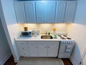 A compact kitchen with white cabinets, a microwave, a sink, and a stove.