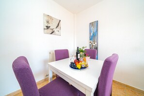 Zona de dinar amb taula blanca, cadires morades i presentació de fruita i suc.
