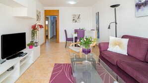 Un soggiorno moderno con una TV a schermo piatto, un tavolino in vetro, un divano viola e un'area pranzo sullo sfondo.