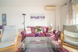 Una sala de estar con una mesa de centro de vidrio, un sofá, una silla y un aire acondicionado instalado en la pared.