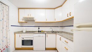 Una cucina con mobili bianchi, lavastoviglie, fornello e lavandino.