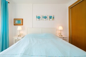 Una habitació d'hotel amb un llit, dues taules de nit amb làmpades, una porta de fusta, un mirall amb una cornisa decorativa i tres quadres de flors penjats a la paret.