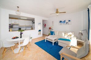 A modern living room with a white sofa, a coffee table, and a dining area with chairs and a table.