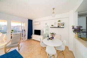 Un salon moderne avec un téléviseur, une table à manger, des chaises et un balcon offrant une vue agréable.
