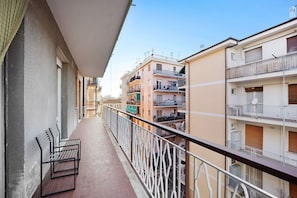 A balcony with two metal benches, a railing, and a view of adjacent buildings.