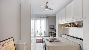 A bedroom with a bed, a ceiling fan, a desk, and a shelf with stuffed animals.