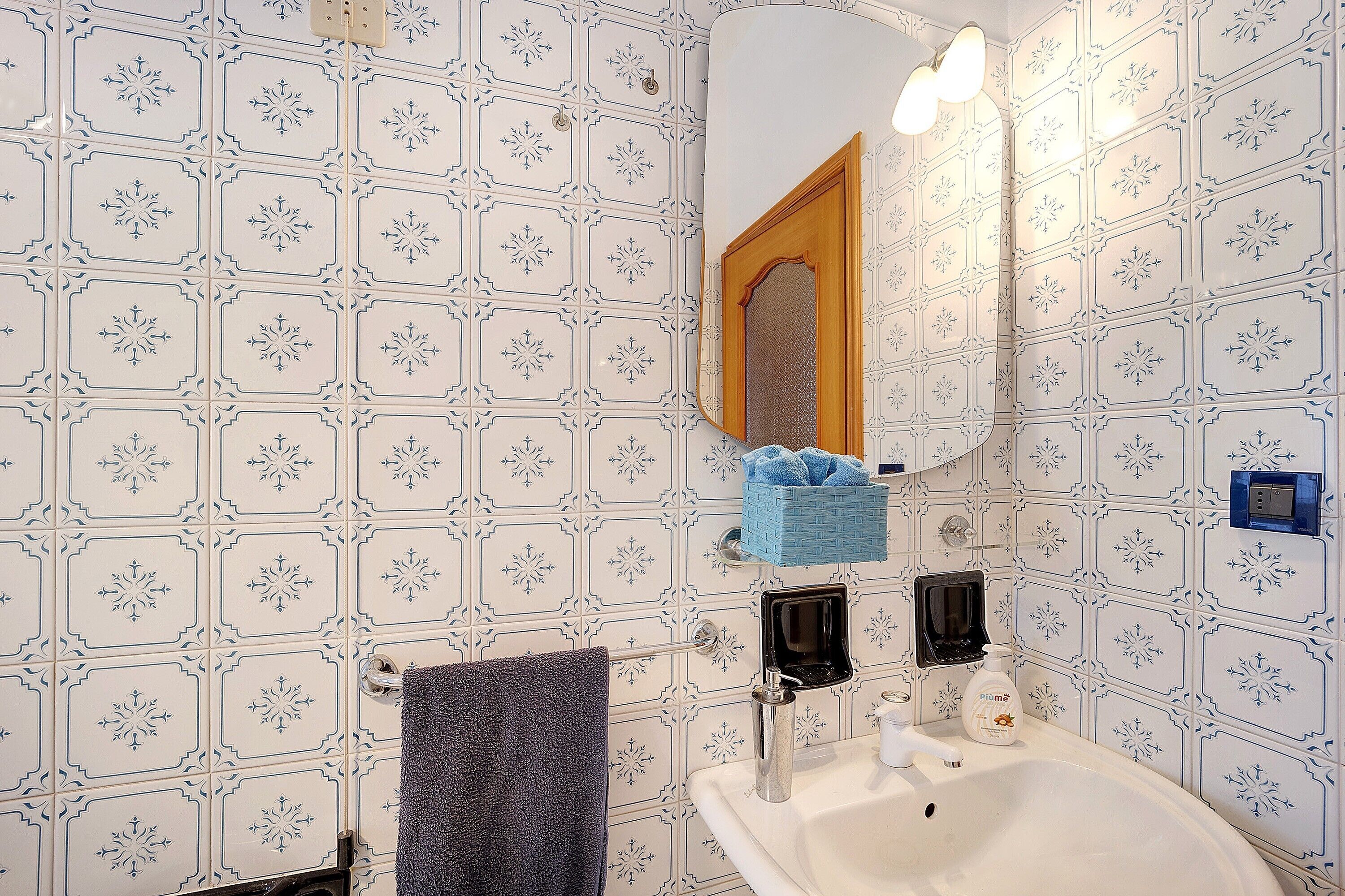 Une salle de bain avec un lavabo blanc, un miroir, un porte-serviettes et un distributeur de savon bleu.