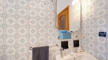 Une salle de bain avec un lavabo blanc, un miroir, un porte-serviettes et un distributeur de savon bleu.