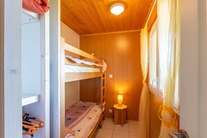 Une chambre avec un lit superposé, un plafond en bois, une petite table avec une lampe et une fenêtre avec des rideaux.