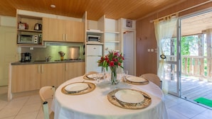 Een eethoek met een tafel voor vier personen, een keuken met apparatuur, en een schuifdeur naar een terras.