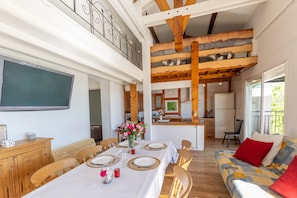 A dining area with a table set for four, a sofa with red cushions, and a kitchen in the background.