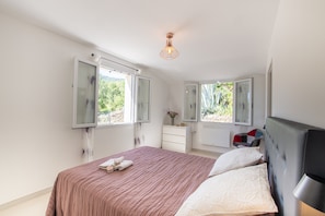 A bedroom with a bed, a dresser, a chair, and a window with an open shutter.
