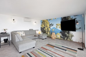 A modern living room with a grey sofa, a small side table, a colorful rug, a mounted TV, and a wall mural.